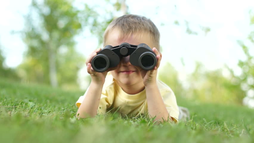 Closeup portrait of a little boy looking through binoculars outdoors
