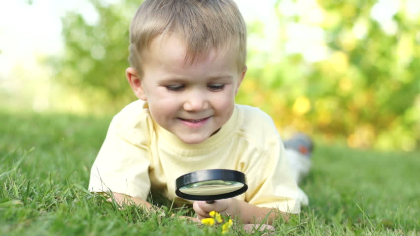 Portrait of a young boy with a magnifying glass lying on the grass
