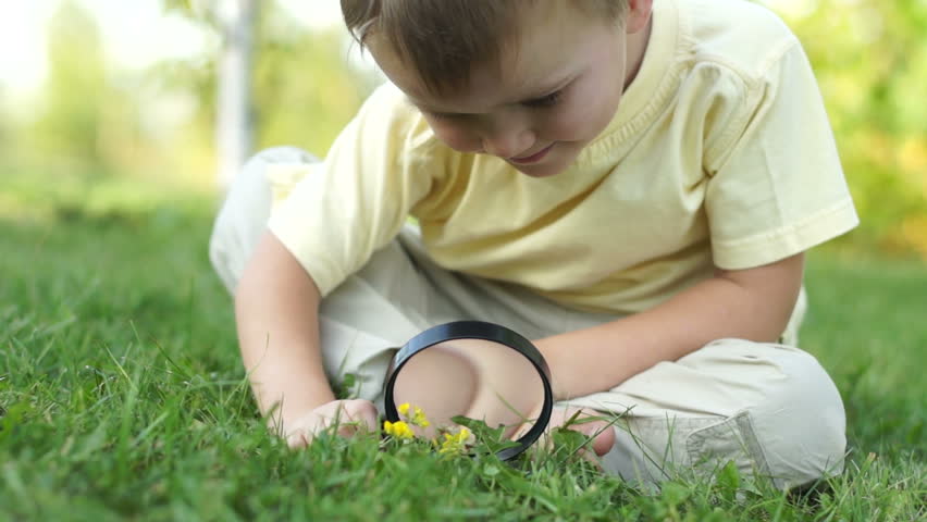 Close-up portrait of a little boy with a magnifier and sitting on the grass

