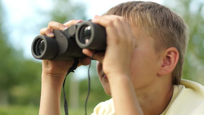 Closeup portrait of a boy looking through binoculars outdoors
