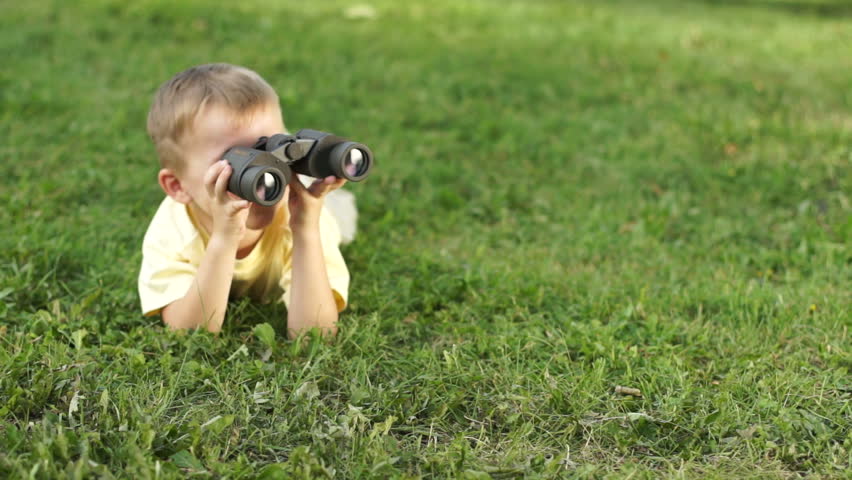 Little boy with binoculars lying on the grass
