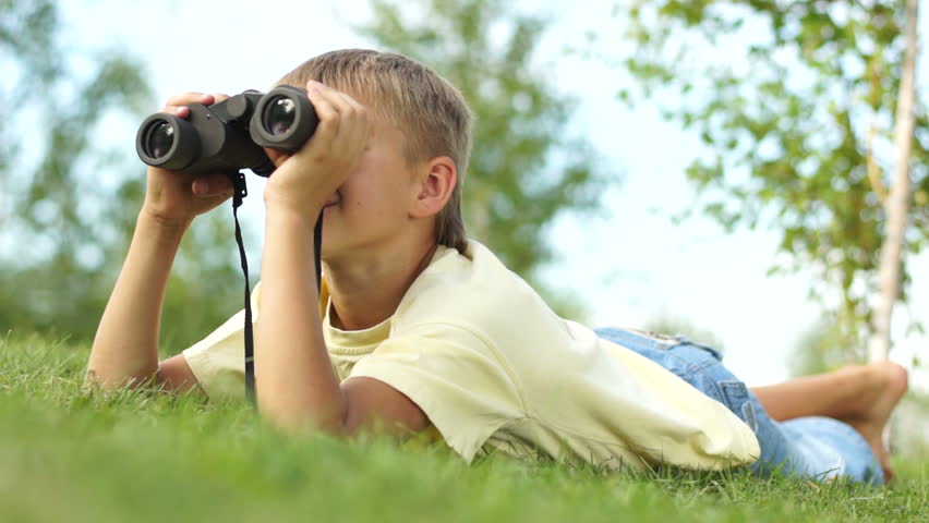 Portrait of a boy looking through binoculars at the camera
