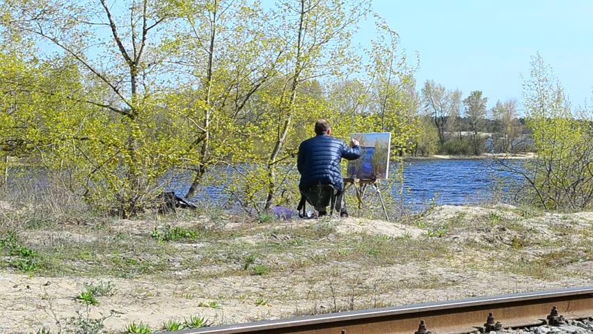 The artist paints a picture on the river bank, during a strong wind