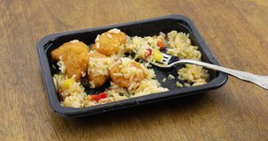 Sweet and sour chicken TV dinner in a black plastic microwavable tray being eaten with a fork on an old wood table top.