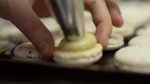 Making macaroons. Chef hands add cream to the ready halves of white macaroons, slow motion, close-up