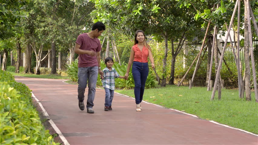 Dolly shot of a happy young Asian family walking together in a park.