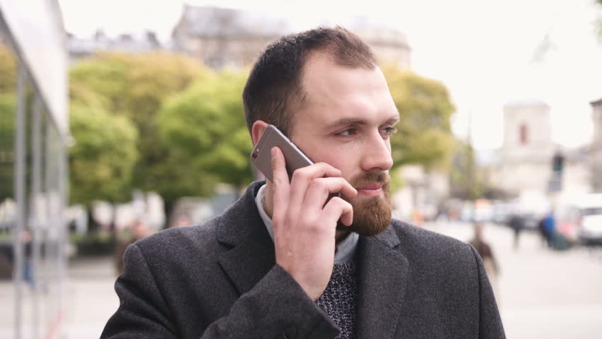Attractive successful man with a beard speaks on the phone and looks to the camera in the city center
