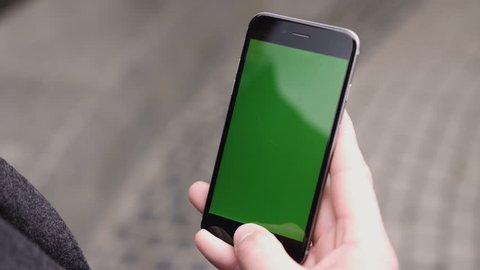 Closeup of a man's hand holding a mobile telephone with a vertical green screen on the streets.