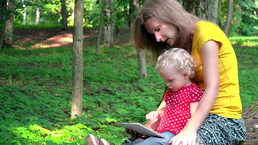 Babysitter woman with cute baby girl using tablet computer in park. 4K