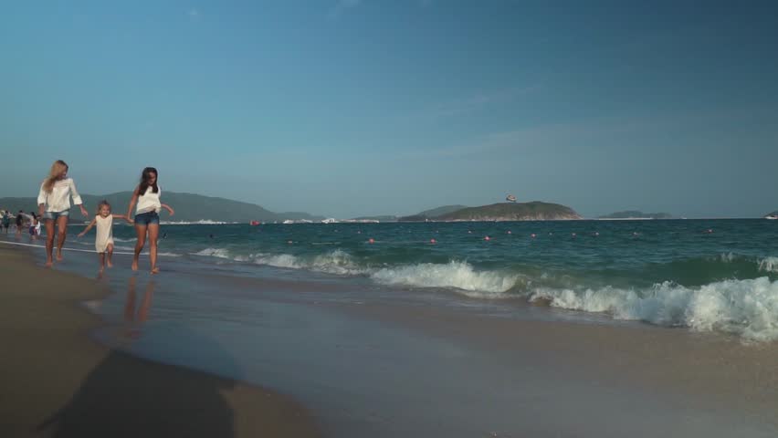 Happy mother with two daughters running along the beach of the South China Sea, Yalong Bay slow motion stock footage video