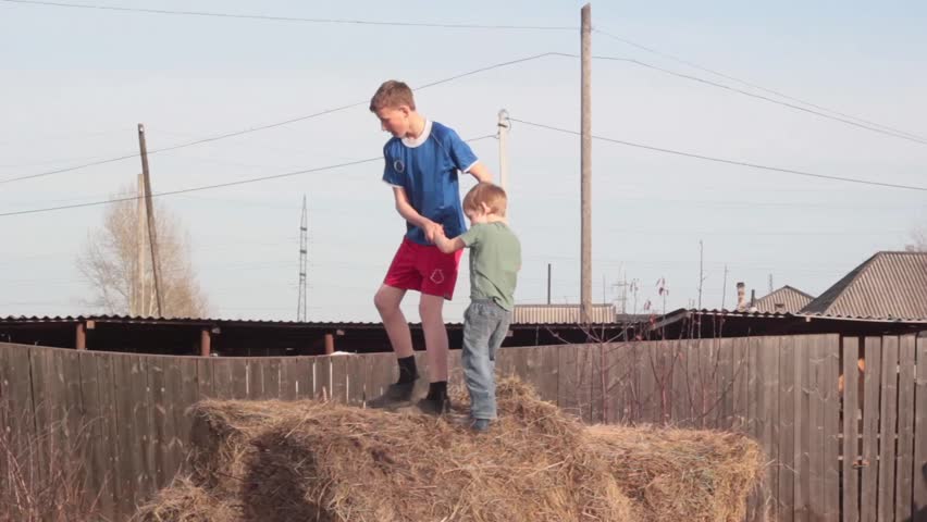 The boy and his younger brother jump in the hay