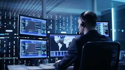 Back View of Technical Controller/ Operator Working at His Workstation with Multiple Displays. Possible Power Plant/ Airport Dispatcher/Government Surveillance. Shot on RED EPIC-W 8K Helium Cinema.