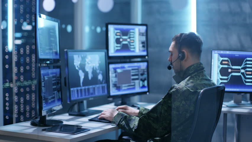 Female and Male Military Technical Support Professional Giving Instructions into Headsets. They're in System Control Room with Many Working Screens.
