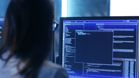 Over The Shoulder Footage of Female IT Engineer Working in Monitoring Room. She Works with Multiple Displays. Shot on RED EPIC-W 8K Helium Cinema Camera.