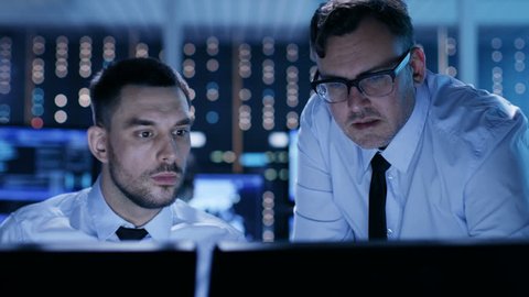 Two Professional Technicians Discussing Problems Shown on Multiple Monitors in a System Control Center.  Shot on RED EPIC-W 8K Helium Cinema Camera.