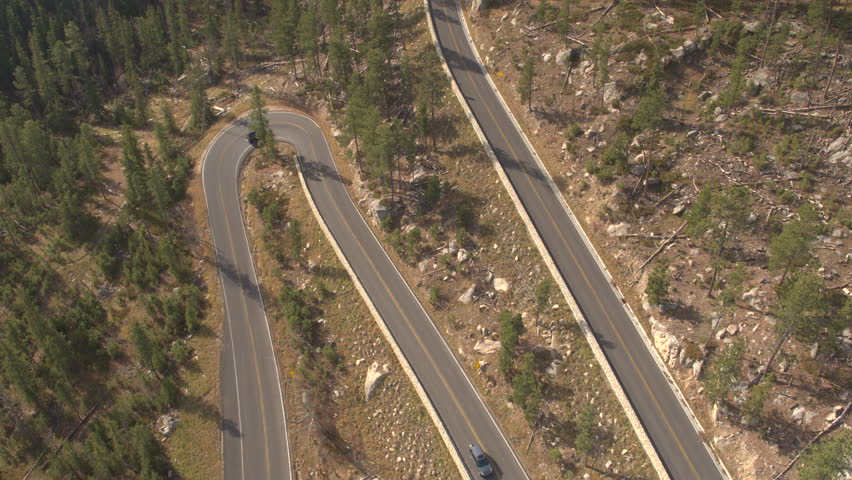 AERIAL: Black SUV jeep and driving along empty snaking mountain pass road in sunny pine forest in Black Hills, USA. People on road trip traveling on curvy switchback highway through rocky countryside