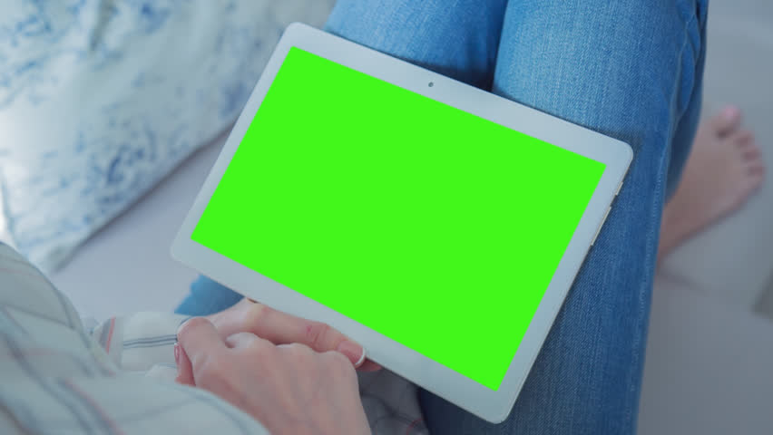 Young Woman sitting on a couch uses tablet PC with pre-keyed green screen. Few types of motion - scrolling up and down, tapping, zoom in and out. Perfect for screen compositing. 10bit ProRes 444