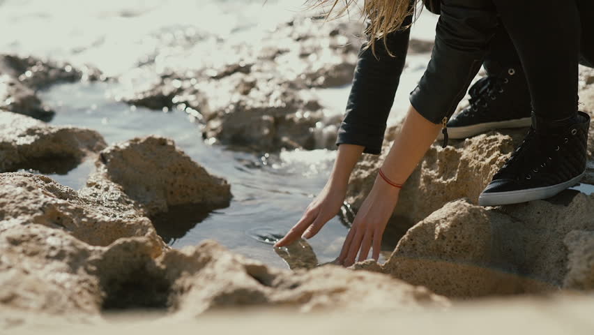 The girl dip her hands into the water on the coast of the sea