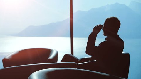 silhouette of businessman with glasses sitting in office lobby looking through the window thinking about finance sales ideas