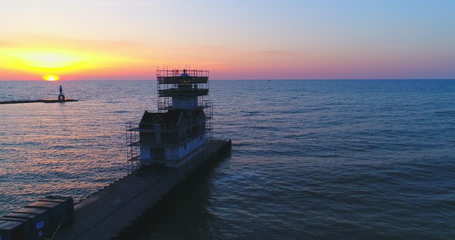 Lighthouse surrounded by scaffolding, under renovation or construction at sunrise. Still doing its job, still beautiful in the dramatic light of dawn.