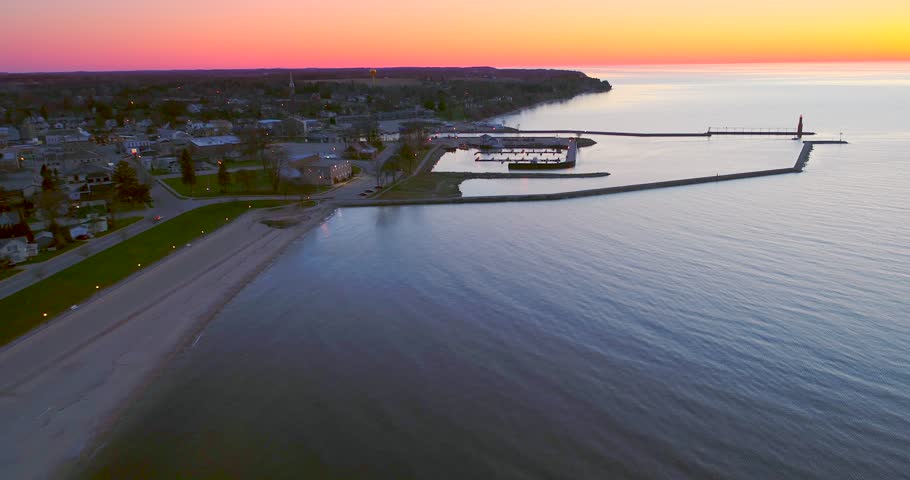 Small fishing boat goes out into Lake Michigan before Sunrise, with iconic Algoma Wisconsin Lighthouse, aerial view
