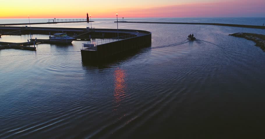Fishing boat motors out before Sunrise into Lake Michigan with iconic Algoma Wisconsin Lighthouse in background.