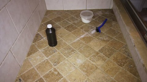Person Scrubbing Shower Tile Floor 
One adult male cleaning grout in a shower tile floor. Low view of a man cleaning a shower tile floor with hydrogen peroxide and baking soda and a small scrub brush.