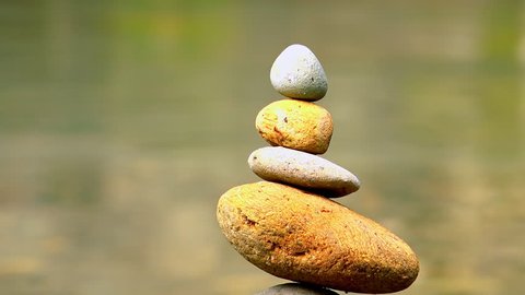 Close-up shot of rocks stacked on top of each other and placed in quiet jungle lake. Meditation scene with stone piles by side of water, balance symbol, harmony and tranquility. Sound of birds singing