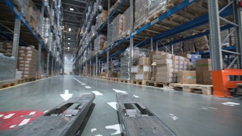 Forklift trucks move between large metal shelves at a modern warehouse. Large warehouse logistics Interior. moves up on shelves of cardboard boxes inside a storage Indoors. Industrial warehouse Lift
