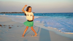 Adorable happy little girl on white beach at sunset. Cute kid dance on the tropical seashore in slow motion video
