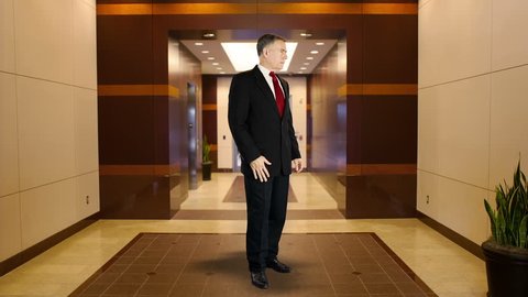 Mature businessman standing in middle of office building lobby area with confident smile and body language.