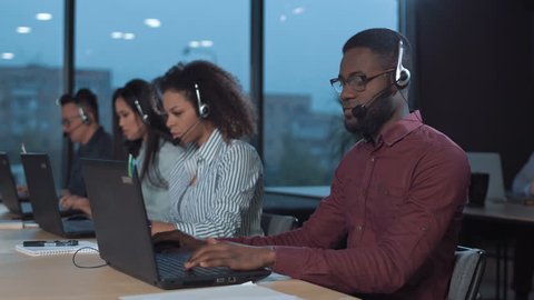 African man with headset working with laptop with other people on the background