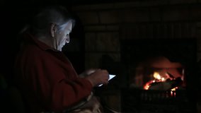 Senior man sits at the fireplace with tablet and watching family video, close-up
