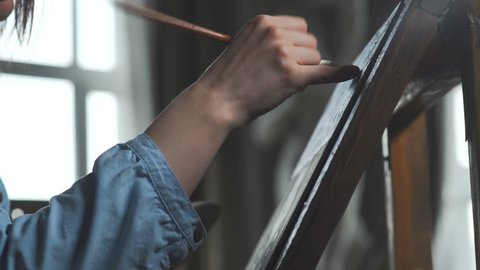 The artist paints a woman on canvas and smears a broad brush. Canvas stands on the easel. The artist draws at the easel. The drawing process: a close-up of the brush and canvas