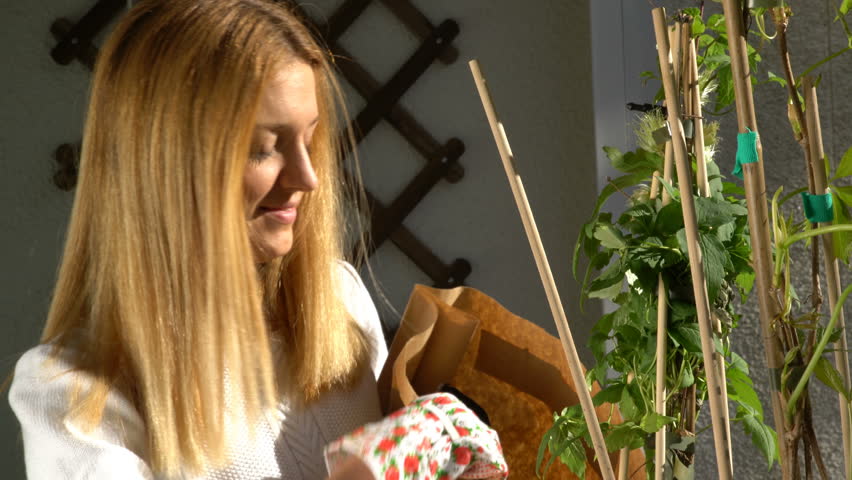 A young woman pours ground in the wooden container and planting the seedlings on the balcony.