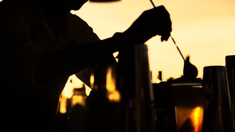 Silhouette of barman preparing cocktail at sunset outside at beach club - video in slow motion