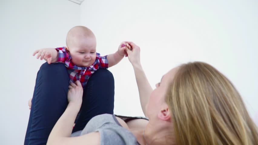 Young mother swinging small baby son on her legs closeup