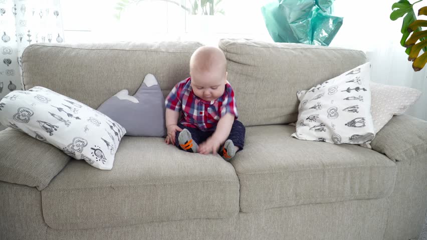 Small cute baby boy sitting on sofa and looking around