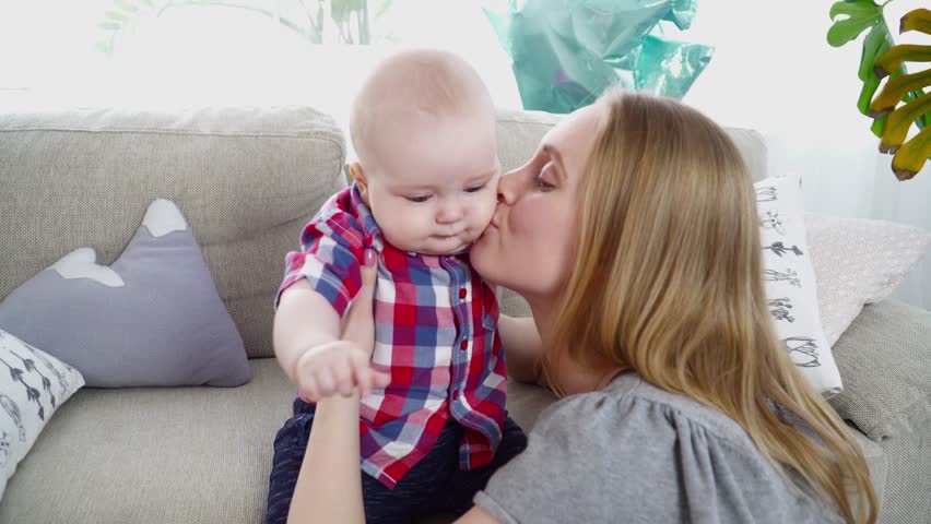 Young mother playing with her 6 months old son while he is sitting on sofa