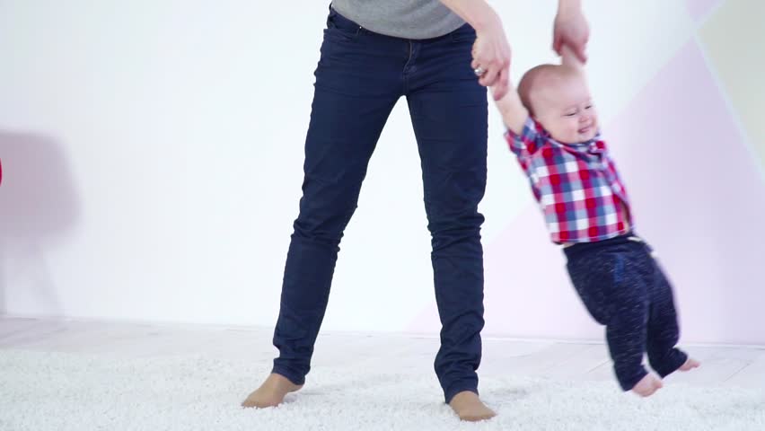 Young mother swinging small baby son on her hands slow motion