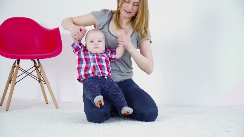 Young mother making exercises with 6 months baby boy in the room