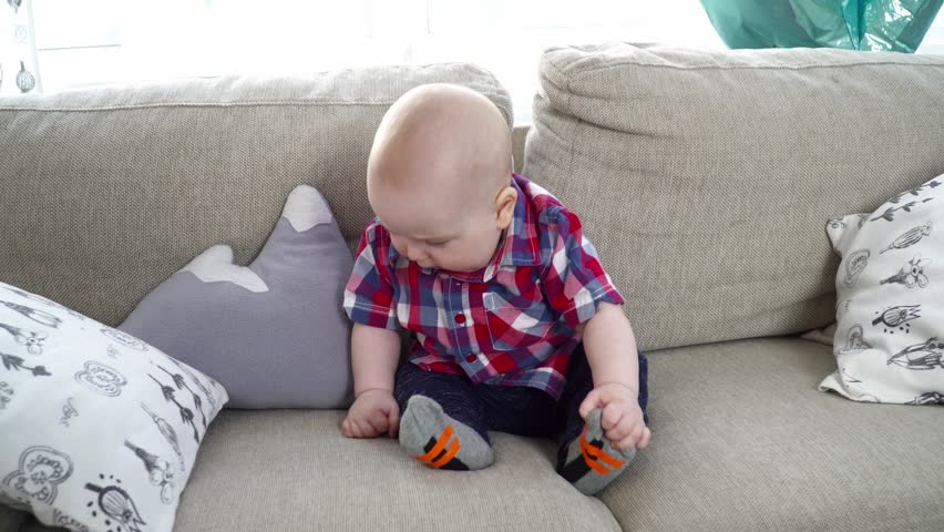 Small cute baby boy sitting and looking around on sofa