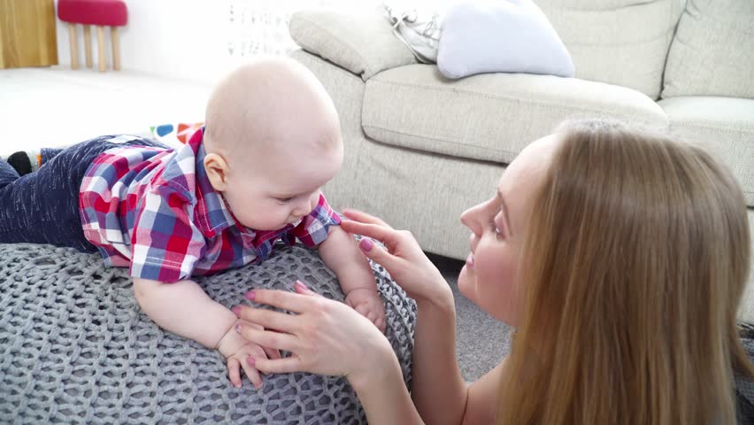 Young mother helping 6 months baby boy to turn closeup