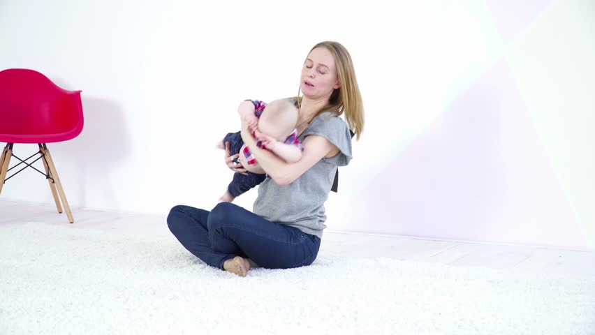 Young mother playing with her 6 months son sitting on carpet