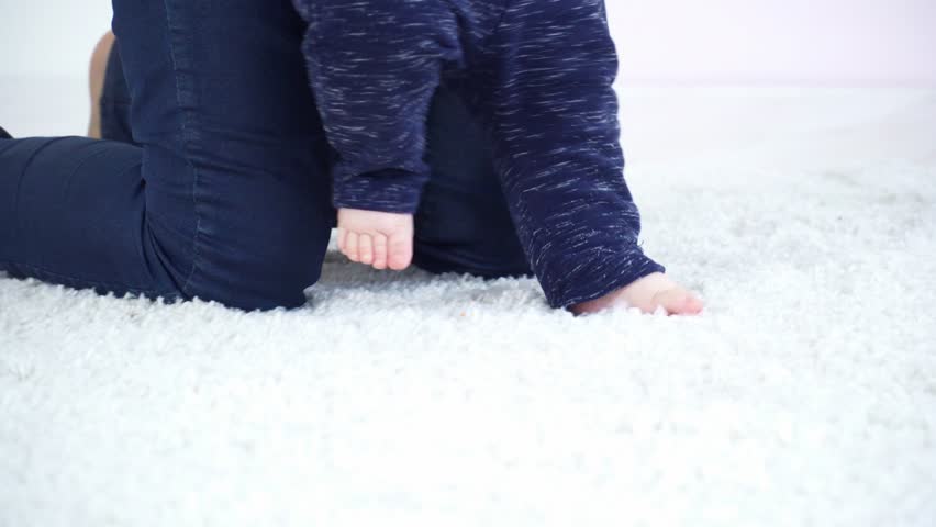 Young mother halping her 6 months to make first steps closeup