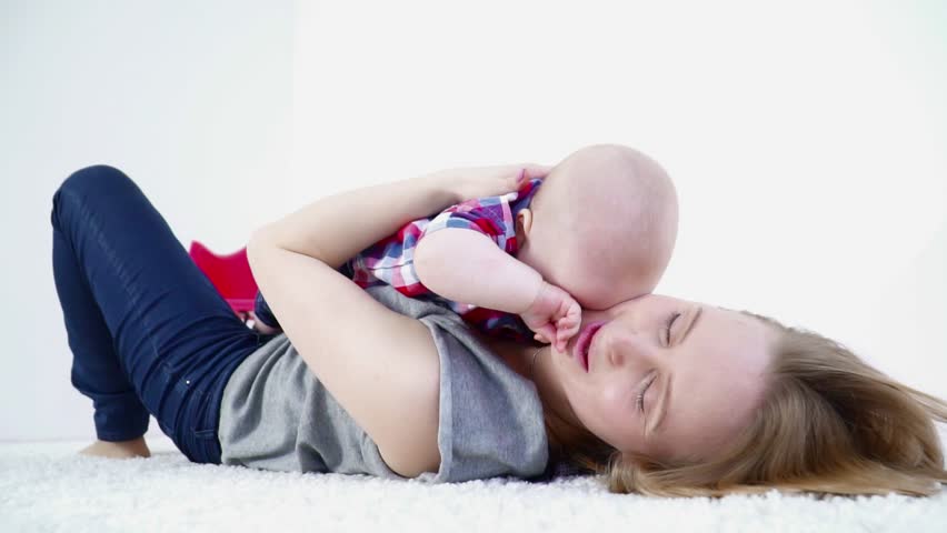 Young mother laying on the carpet with her baby boy laying on her chest slow motion closeup