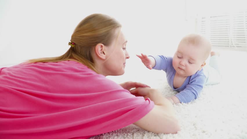 Young mother helping her 6 months son to crawl on floor, first step