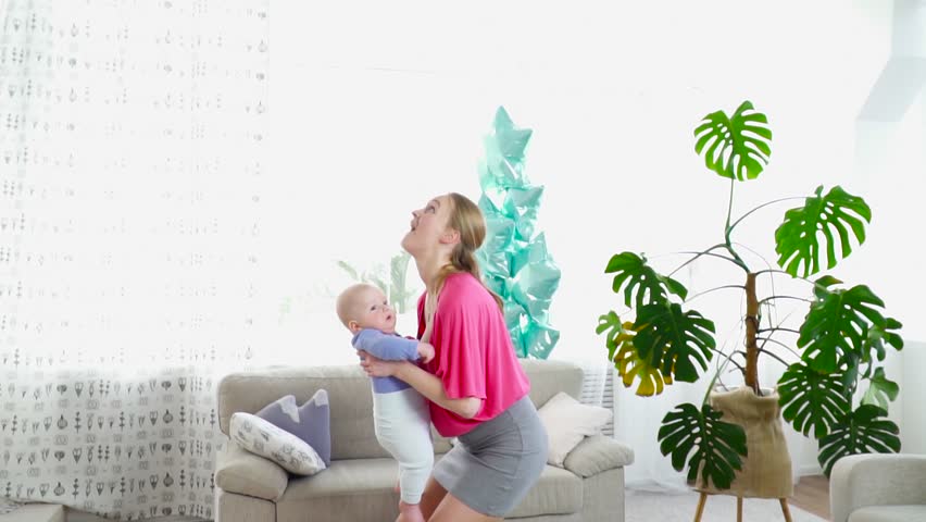 Pretty young mother playing with 6 months son throwing him up slow motion