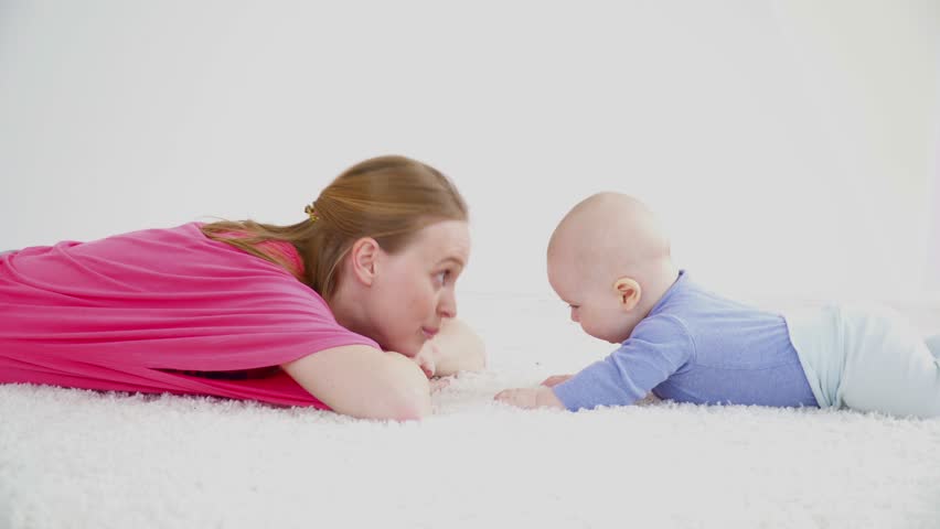 Young mother laying on carpet with her son of 6 months old closeup