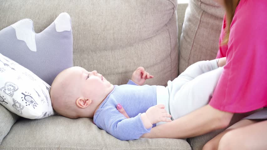 Young mother playing with her 6 months son sitting on sofa closeup